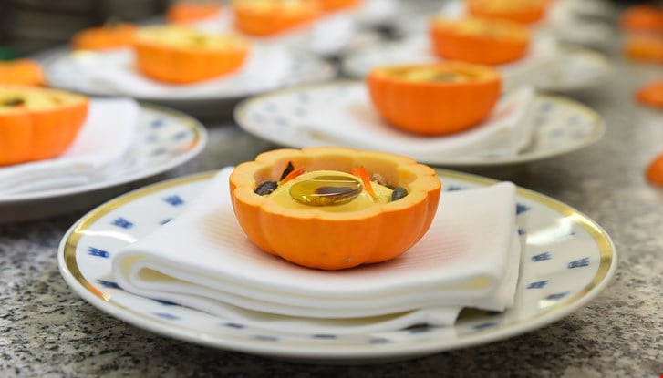 Semifreddo de potimarron servi dans la peau d'un potimarron sur une assiette blanches avec des couronnes bleues.